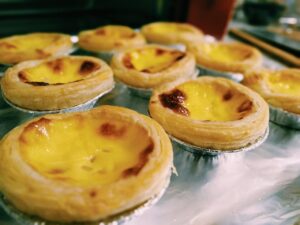 Golden Chinese egg tarts on a bamboo steamer with cracked crusts revealing yellow custard.